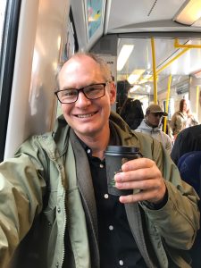 Glad Emil Erdtman med kaffe i pappersmugg. Selfie tagen i tunnelbanan.