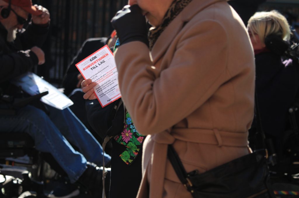 En hand håller ett solupplyst flygblad med rubriken "gör konventionen till lag" medan en annan person passerar.